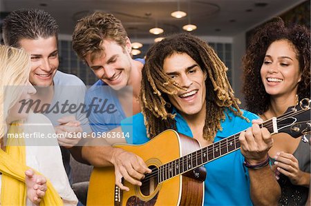 Mann sitzt mit seinen Freunden und eine Gitarre spielen