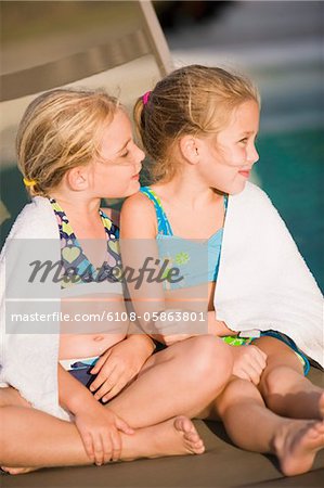 Two girls sitting on a lounge chair at the poolside