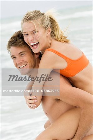 Man giving woman piggyback ride on the beach