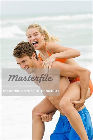 Man giving woman piggyback ride on the beach