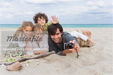 Homme qui prend une photo de sa famille avec un appareil photo numérique sur la plage