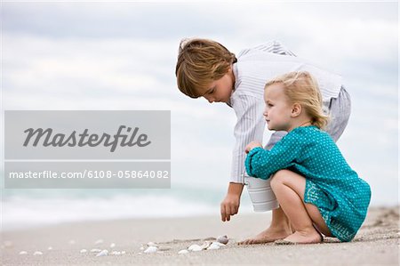 Boy and his sister playing with shells on the beach
