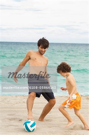 Boy playing soccer with his father on the beach