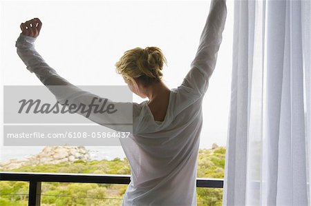 Vue arrière d'une femme qui s'étend ses bras au balcon