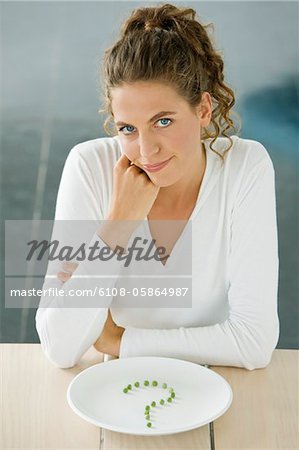 Frau sitzt an einem Tisch mit Erbsen in Frage markieren Form auf einem Teller