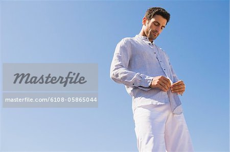 Man buttoning shirt on the beach