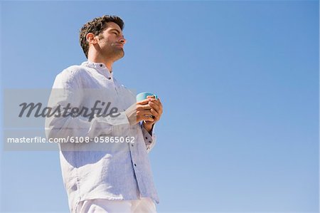 Man holding a cup of coffee on the beach