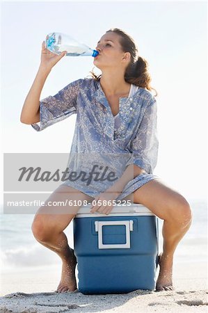 Femme assise sur un compartiment à glace et l'eau potable sur la plage