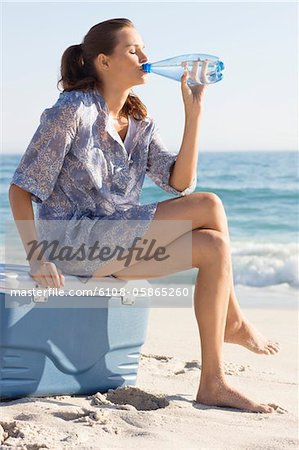 Woman sitting on an ice box and drinking water on the beach