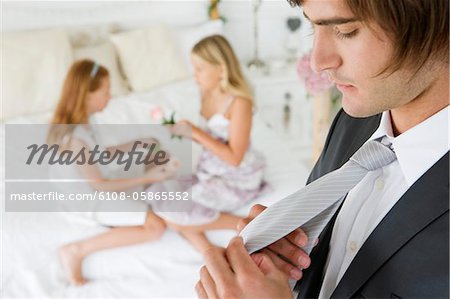 Groom adjusting his tie with two girls in the background
