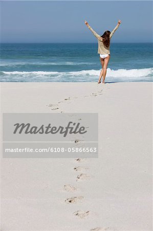 Rear view of a woman standing on the beach with her arms raised