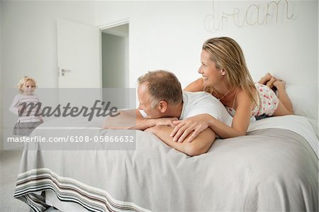 Couple lying on the bed and looking at their daughter