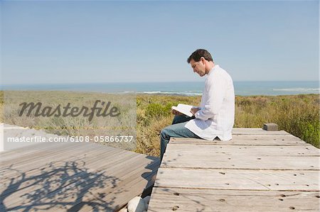 Homme assis sur un trottoir de bois et de lire un livre