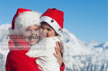 Mutter und Dauhter tragen Santa Hüte, umarmen