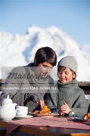 Mère et fille mangeant sur balcon donnant sur la station de ski