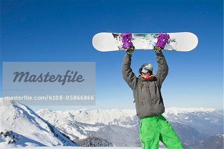 Young man holding his snowboard above his head