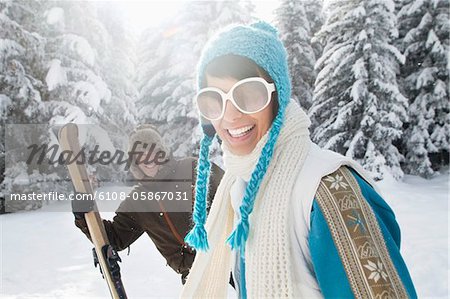 Young woman in winter clothes smiling at camera, man holding skis in background