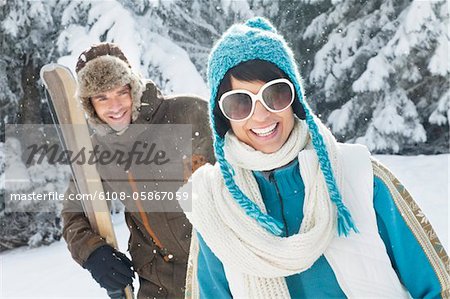 Junge Frau in Winterkleidung lächelnd in die Kamera, Mann, Ski im Hintergrund hält
