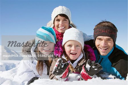 Parents et enfants se trouvant dans la neige, souriant à la caméra