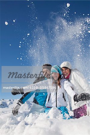 Couple et fille dans des vêtements de ski, jets de neige dans l'air