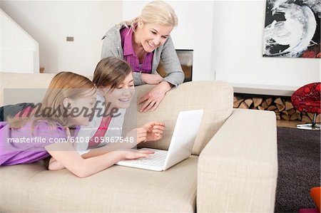 Two girls using a laptop on a couch with their grandmother standing beside them