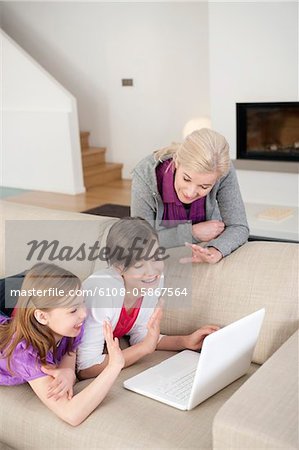 Deux jeunes filles, à l'aide d'un ordinateur portable sur un canapé avec leur grand-mère debout à côté d'eux