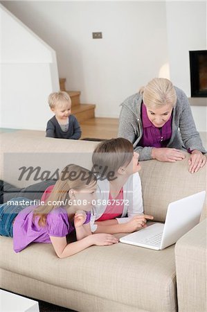 Zwei Mädchen mit einem Laptop auf der Couch mit ihrer Großmutter