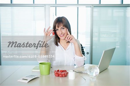 Geschäftsfrau hält eine Kirschtomate und Lächeln