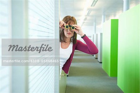 Femme regardant à travers les jumelles dans un couloir de bureau