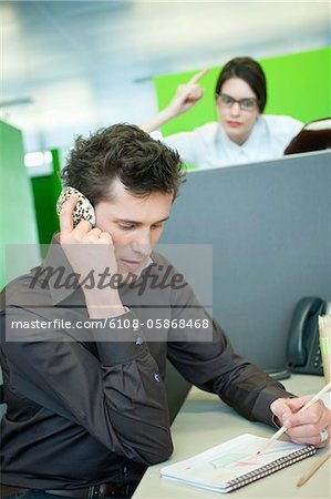 Businessmen talking on a mobile phone while his colleague looking angry