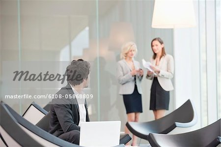 Businessman sitting in a waiting room looking at his colleagues standing in the background