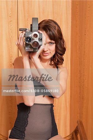 Young woman in underwear using old-fashioned movie camera