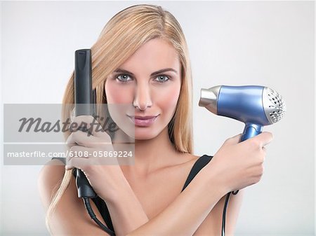 Jeune femme à l'aide du lisseur à cheveux et sèche-cheveux
