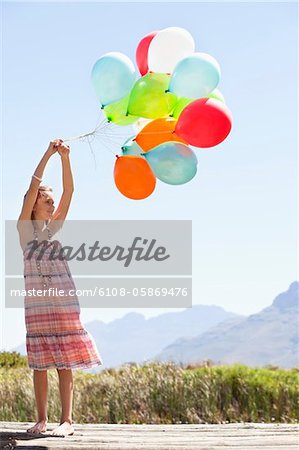 Girl playing with balloons at a pier