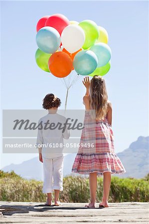 Rear view of siblings playing with balloons at a pier