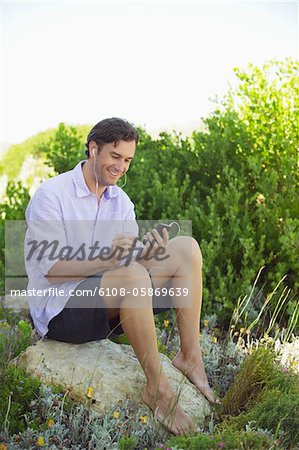 Mid homme adulte assis sur un rocher et écouter de la musique avec un lecteur MP3