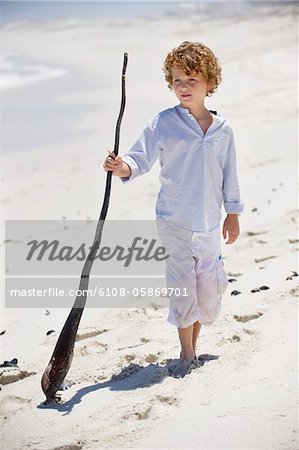 Boy standing with a wooden stick on the beach