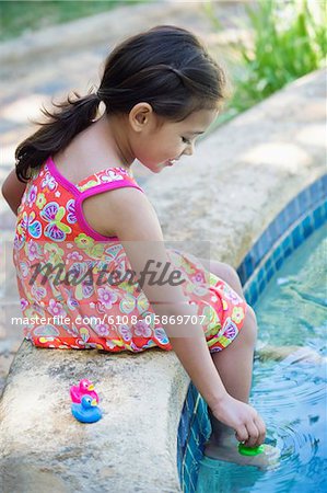 Mädchen spielen mit Gummienten am Rand des Swimmingpools