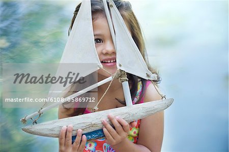Little girl sitting by the swimming pool with model of boat in hand