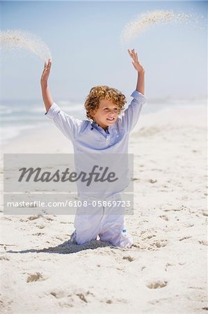 Boy playing in sand with his arms raised