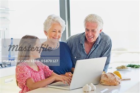 Girl using a laptop with her grandparents looking at her in a kitchen