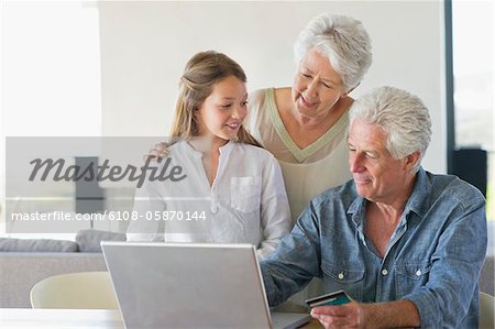 Senior man doing home shopping with a credit card with his family near him
