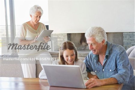 Mann mit einem Laptop mit seiner Enkelin und seine Frau auf eine digitale Tafel im Hintergrund arbeiten