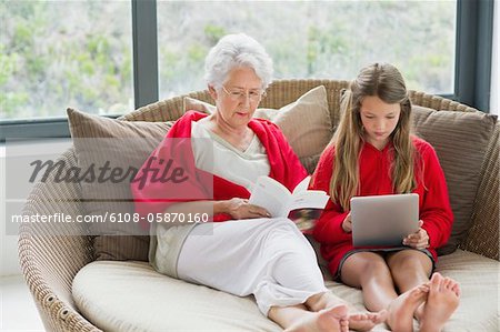 Senior woman reading a magazine with her granddaughter using a digital tablet