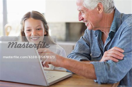 Homme montrant un ordinateur portable à sa petite-fille et souriant
