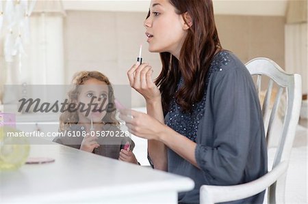 Jeune femme et petite fille appliquant le brillant à lèvres à la coiffeuse