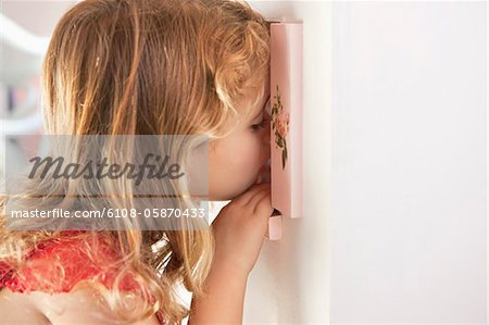 Cute little girl peeking into a dollhouse through the window