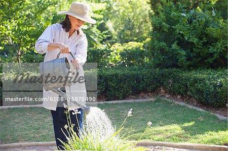 Senior woman in straw hat watering plants in a garden