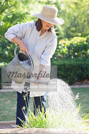 Senior Woman in Strohhut Bewässerung von Pflanzen in einem Garten