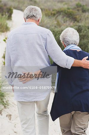 Rückansicht des ein altes Paar, Wandern am Strand mit ihren Armen umeinander